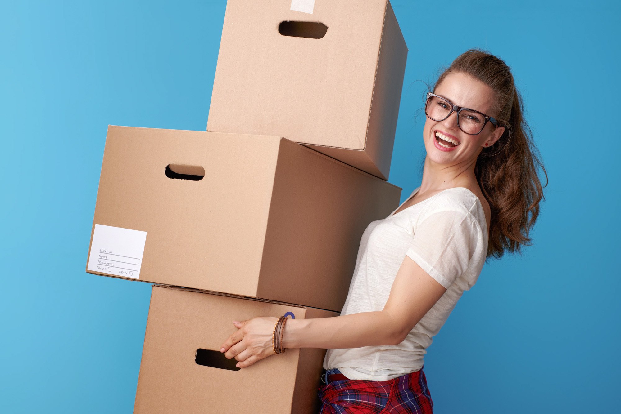 Woman carrying three packing cartons and smiling intensely