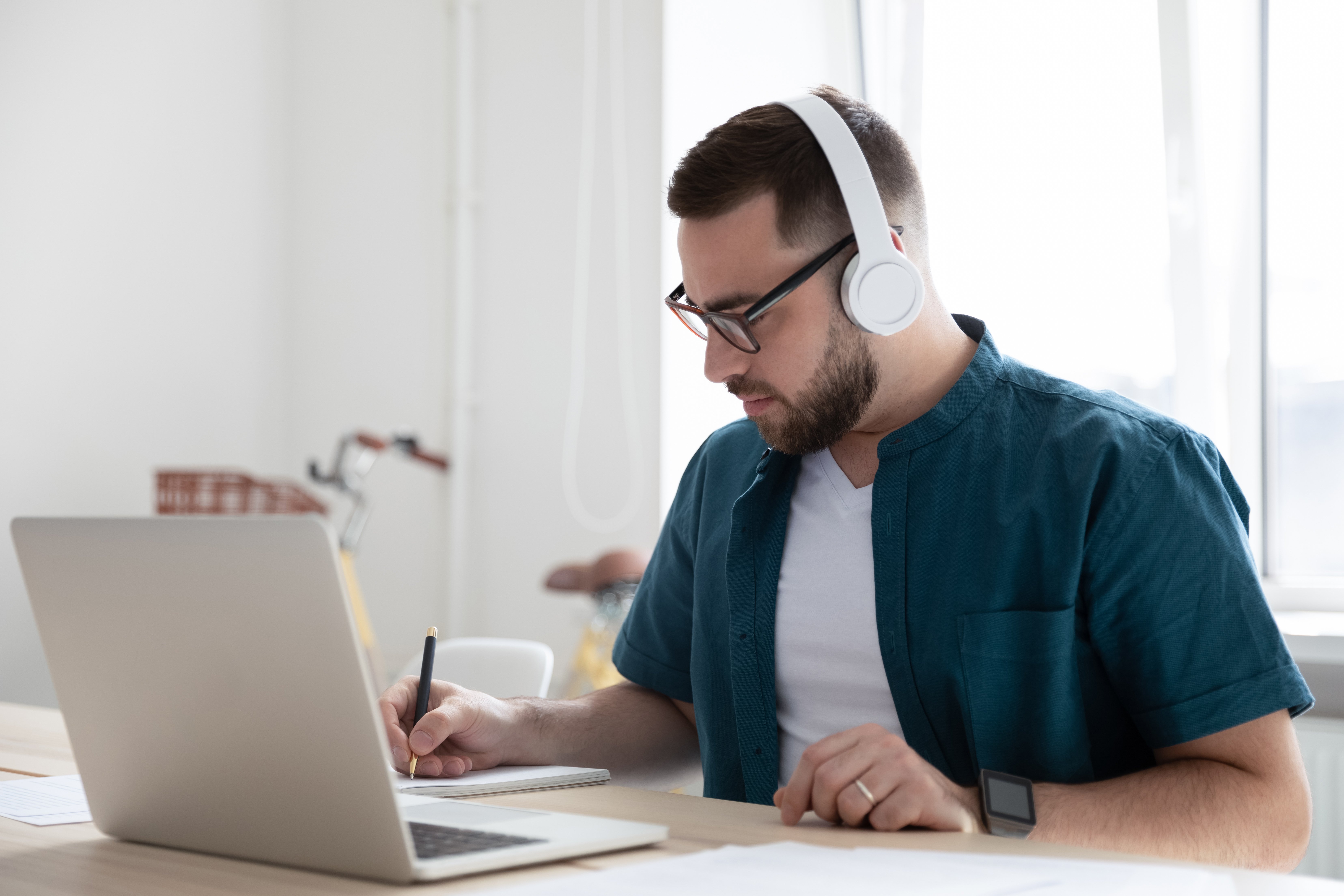 Man working at a laptop, possibly at home, with white wireless headphones on.
