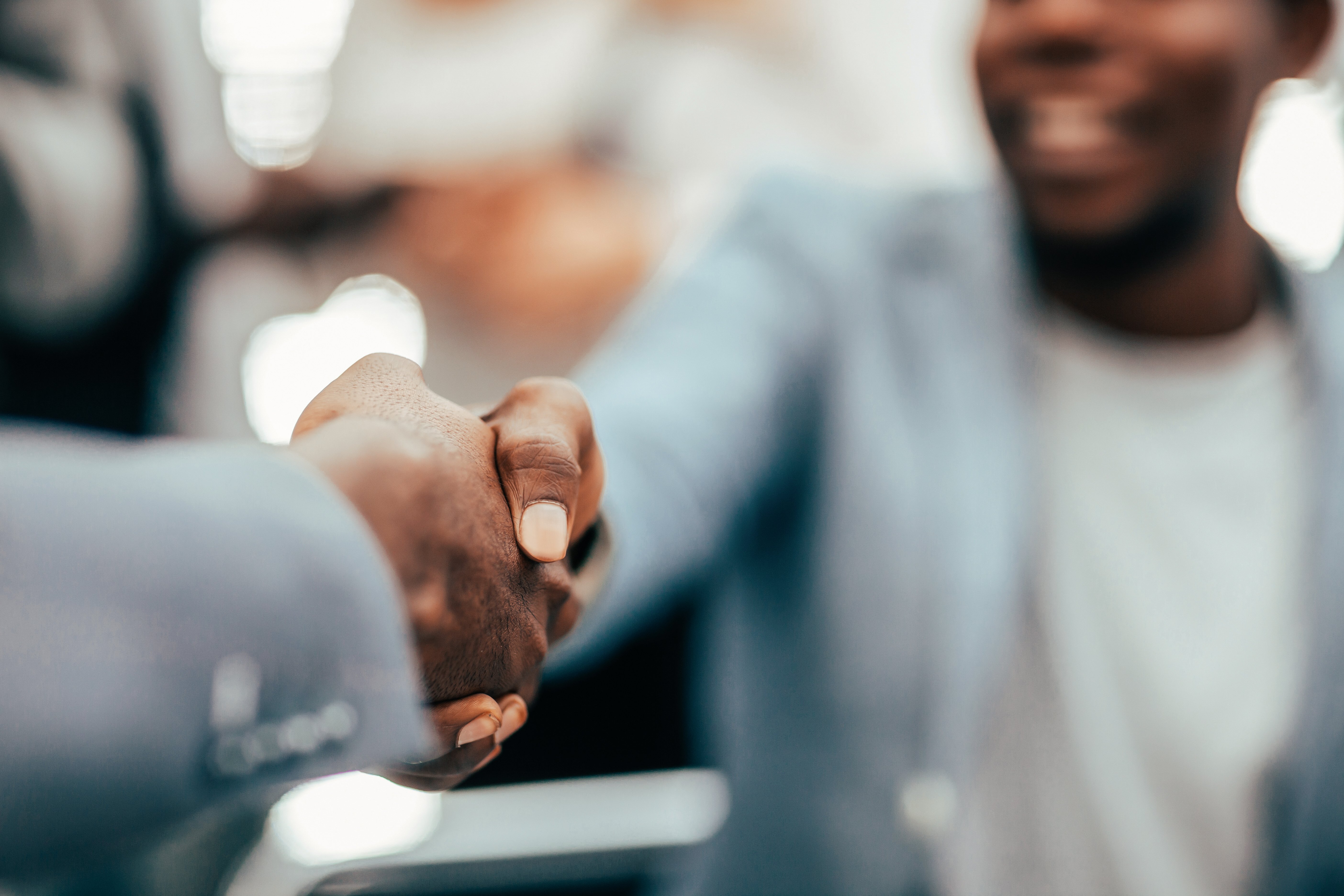 Black man in a suit jacket and t-shirt shakes hands with another man we can't see