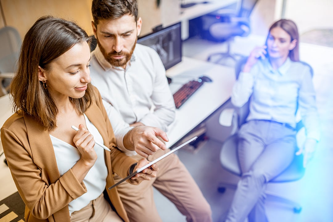 Woman in a beige suit is showing a man something on a tablet