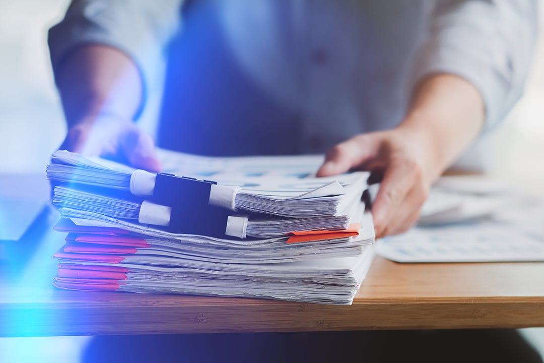 Man's hands holding stacks of various papers held together with bulldog clips, looks like archive material representing historical data ready for a data lake